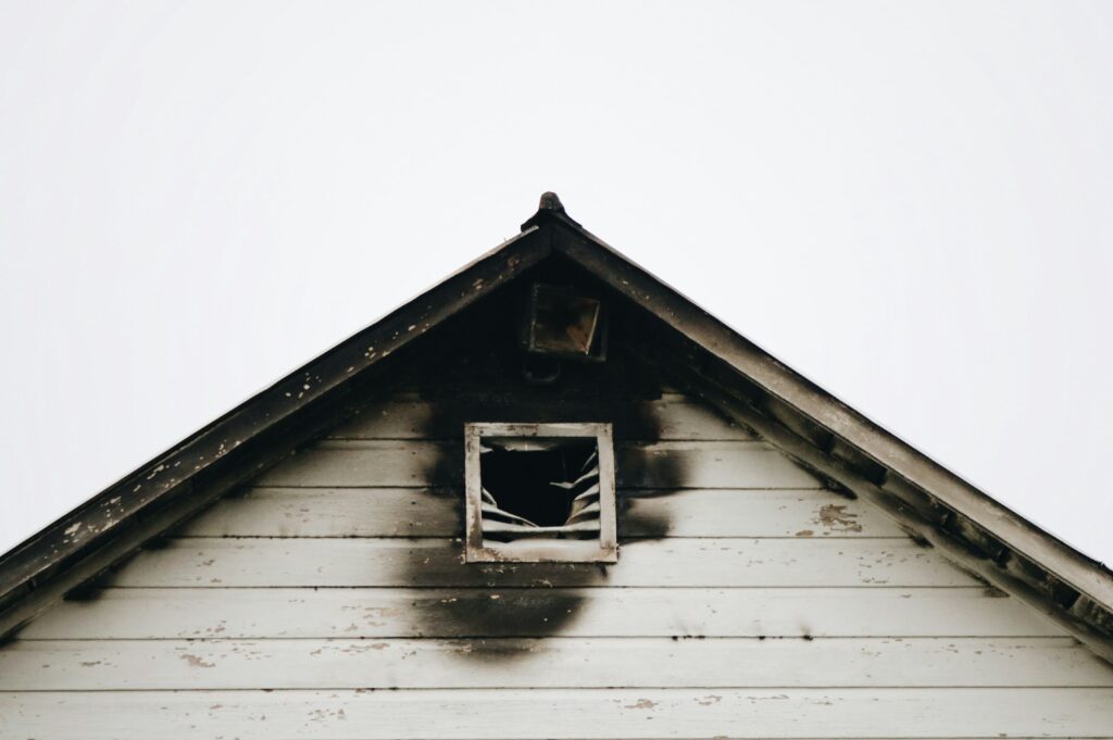 The exterior of a white home with fire damage outside of the attic window