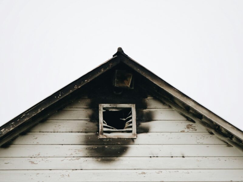 The exterior of a white home with fire damage outside of the attic window